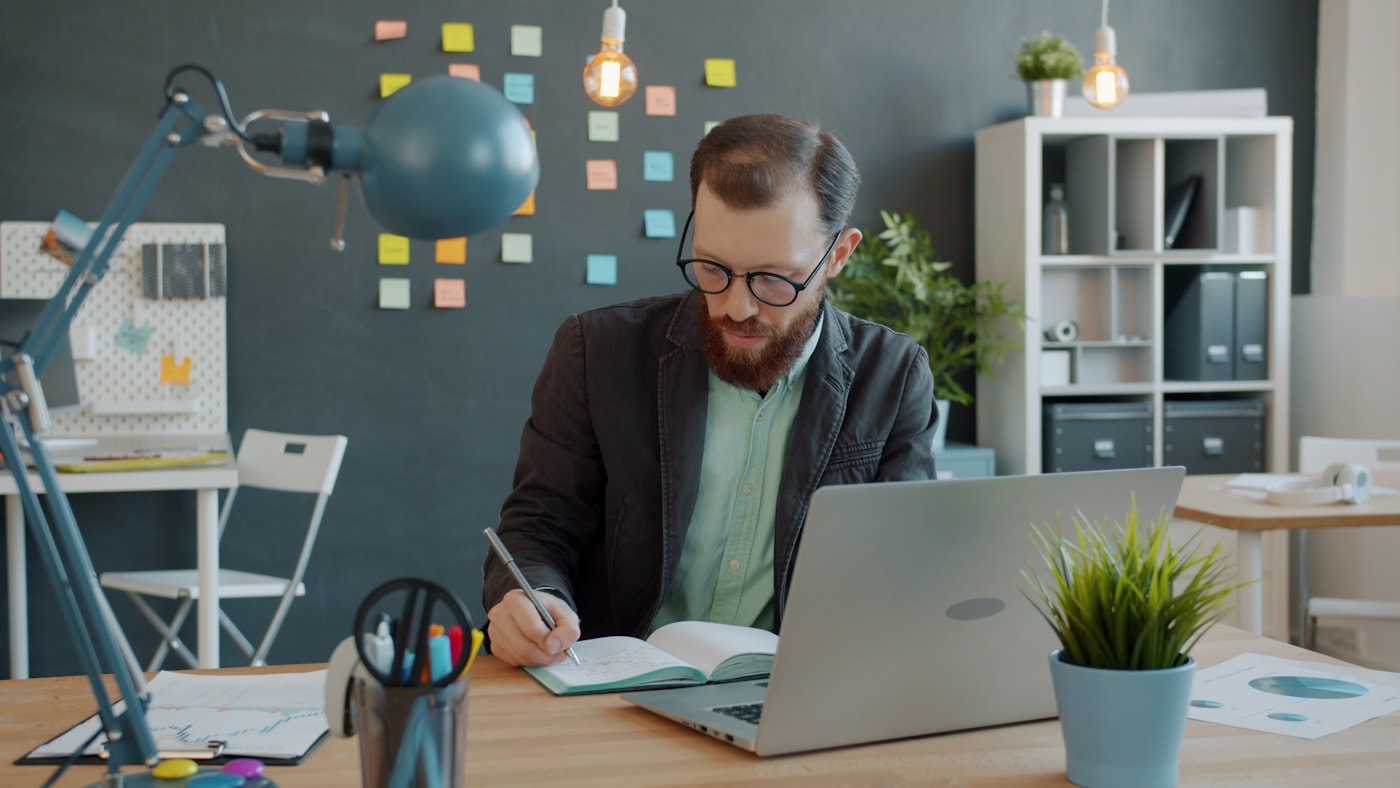 A professional mapping priorities in a notebook beside a laptop